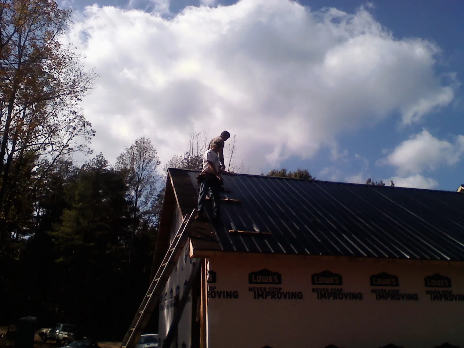 Roofer fastening dark metal panels high against a cloudy sky, from a Roof Inspection job in Kingman